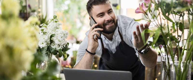 Florist som pratar i telefonen, omgiven av blommor